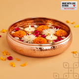 Copper-finish hammered urli with flowers, petals and three floating tealights, styled for Diwali