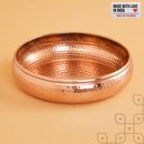 Empty hand-hammered copper-finish urli bowl against a cream background