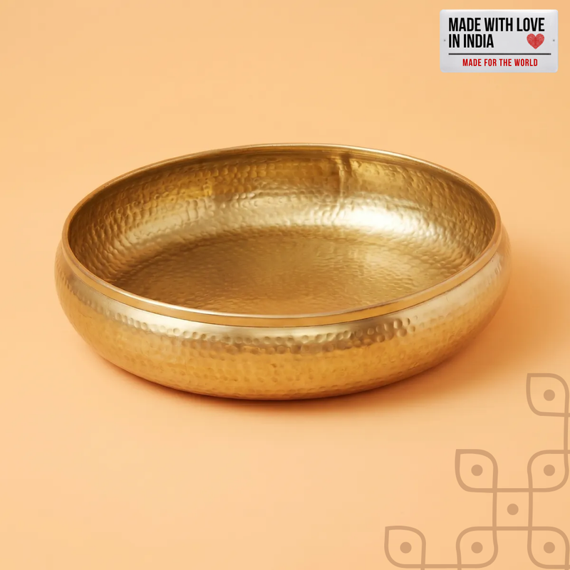 Empty hand-hammered brass-finish urli bowl against a cream background